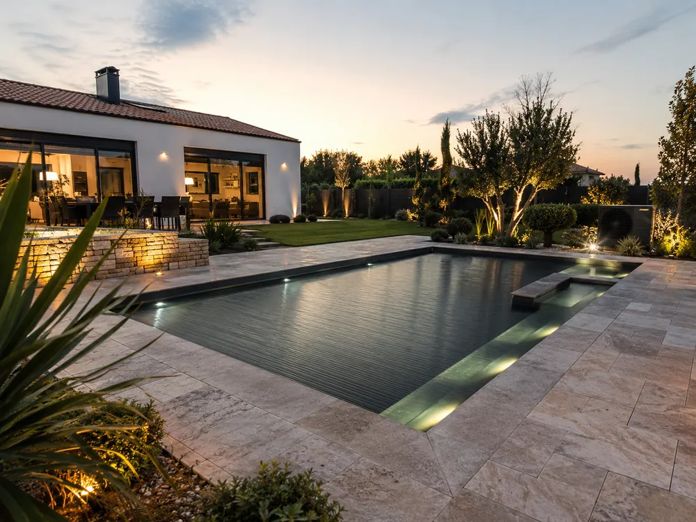 Piscine sur mesure illuminée au crépuscule dans un jardin paysager